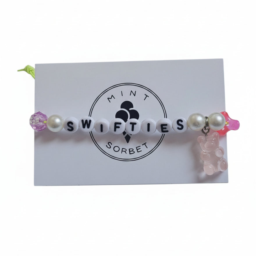 Handmade Swifties friendship bracelet with letter beads, pink glass beads and gummy bear charm on Mint Sorbet packaging card