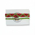 Red and green hand-knotted cotton friendship bracelet set with chevron pattern and green cord bracelet with silver cowrie shell charm on Mint Sorbet packaging card