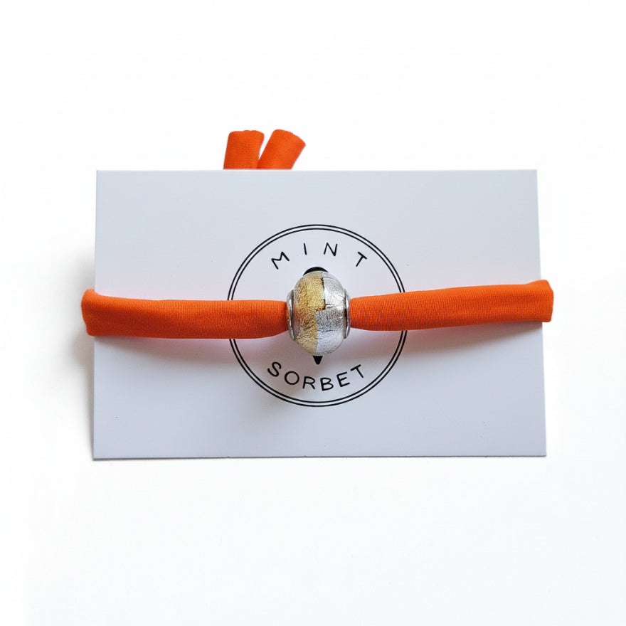 Orange elastic bracelet with gold and silver Murano glass bead on Mint Sorbet packaging card