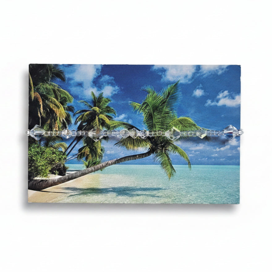 Clear Swarovski crystal beaded bracelet with iridescent bicone beads on tropical beach packaging card